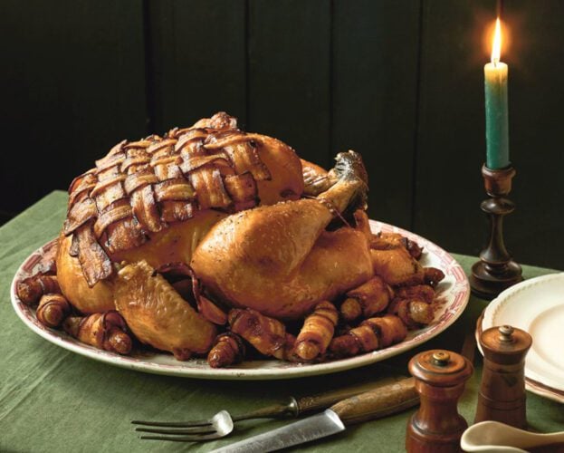 A roast turkey with a bacon lattice over the breast, displayed on a dining table