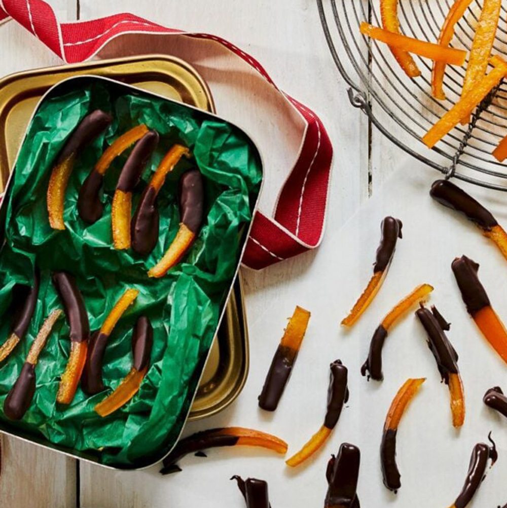Chocolate-dipped candied orange peels laid out on a surface and layered into a box for Christmas hamper ideas