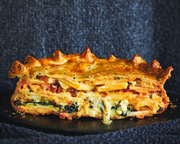 A large golden pie sliced open, revealing slices of veg and oozing cheese