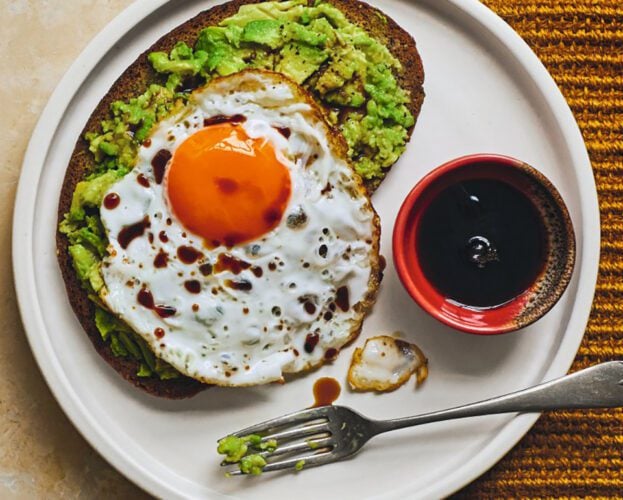 A plate with toast topped with avocado and a fried egg, and a small bowl of soy sauce on the side