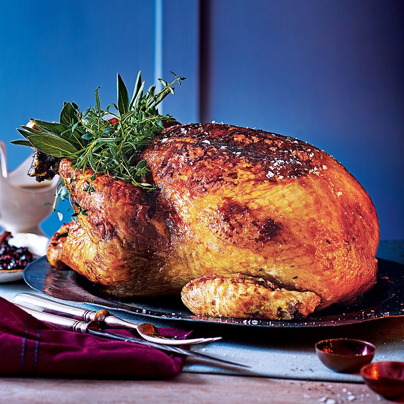 A roasted turkey, garnished with fresh herbs, on a dining table 