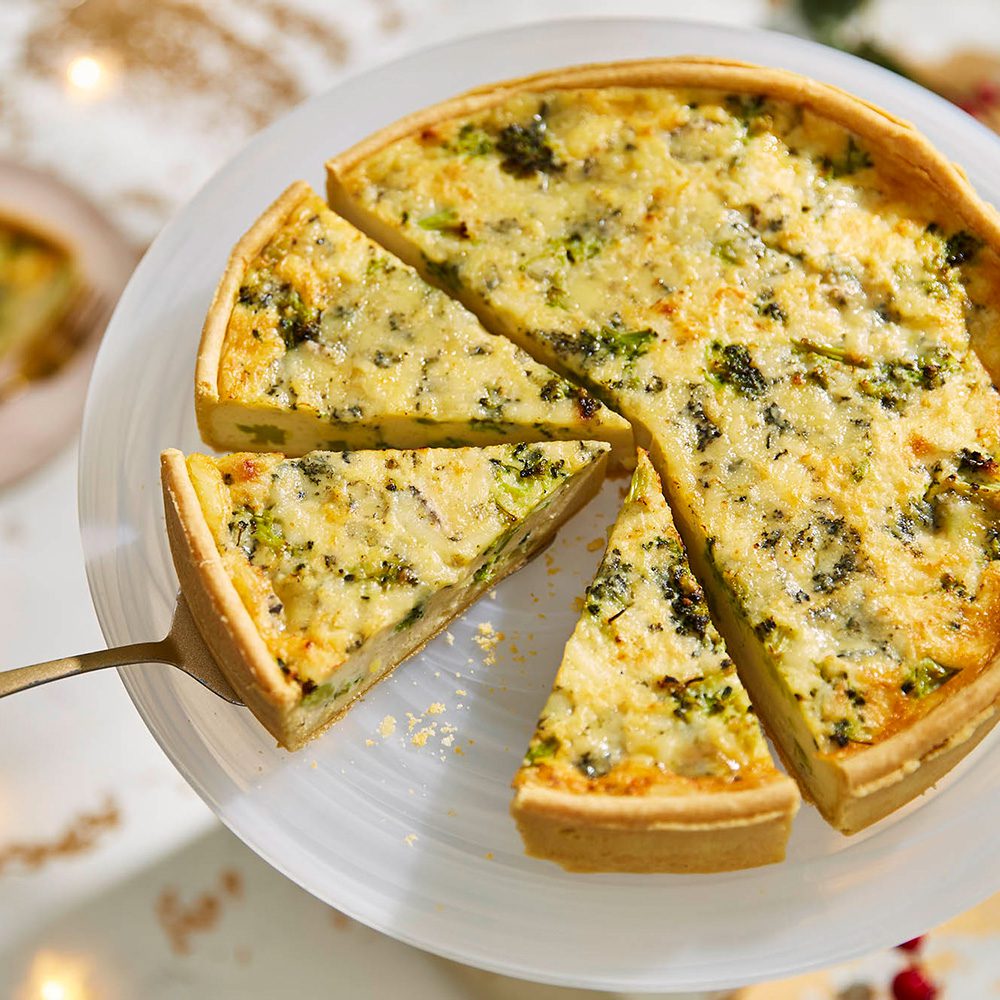 A cheese and broccoli quiche, partly sliced into portions