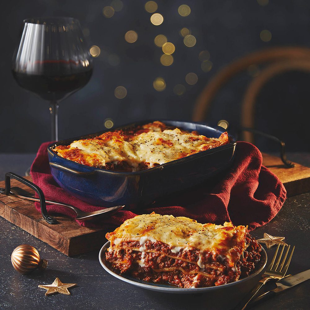 A serving dish of lasagne with a portion on a plate