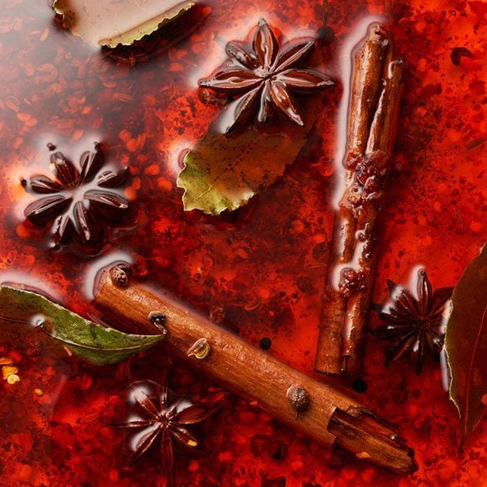 A close up of the surface of chilli oil with. star anise and cinnamon sticks floating in it for Christmas hamper ideas