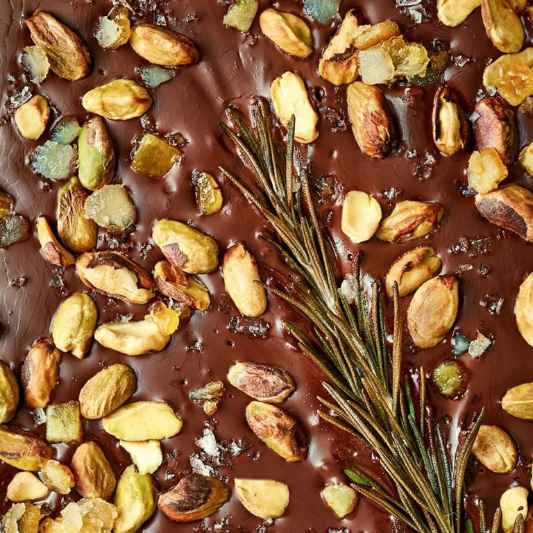 A close-up of dark chocolate studded with pistachios and a sprig of rosemary, for Christmas hamper ideas