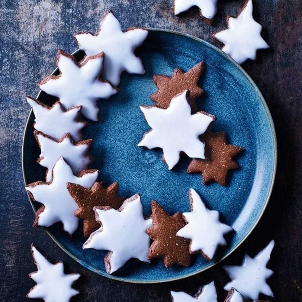 Star-shaped lebkuchen biscuits with white icing spilling off a plate onto the table, for Christmas hamper ideas
