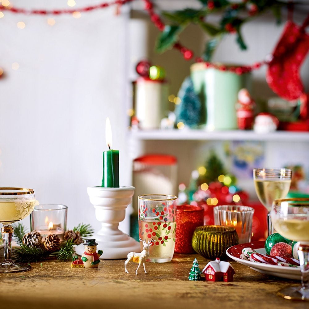 A table strewn with Christmas items including drinks glasses, retro Christmas cake decorations and candles