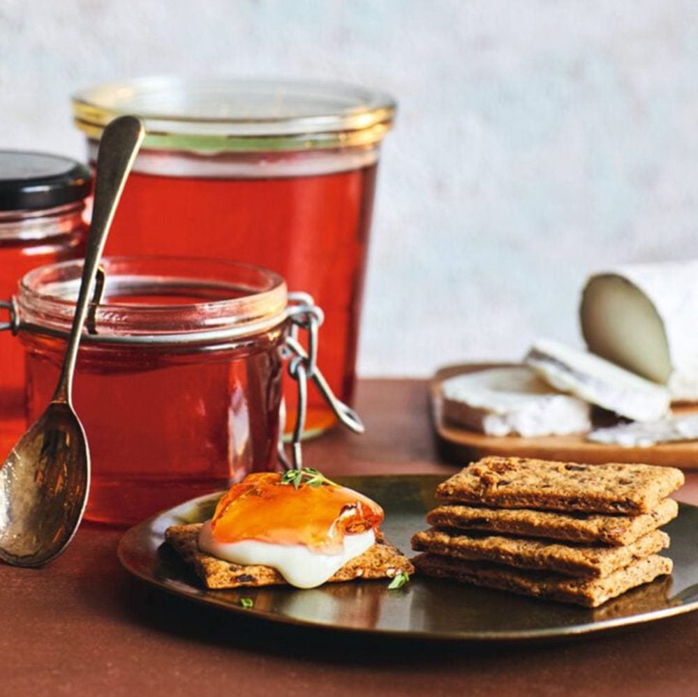 Wine jelly, spread on a cracker with cheese in the foreground, and in jars in the background for Christmas hamper ideas
