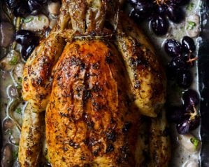A bronzed roast chicken on a bed of roasted bean and grapes