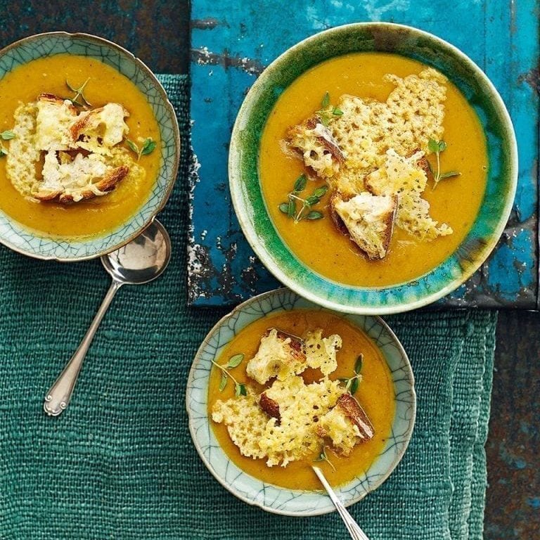 An overhead view of three bowls of squash soup topped with cheddar croutons