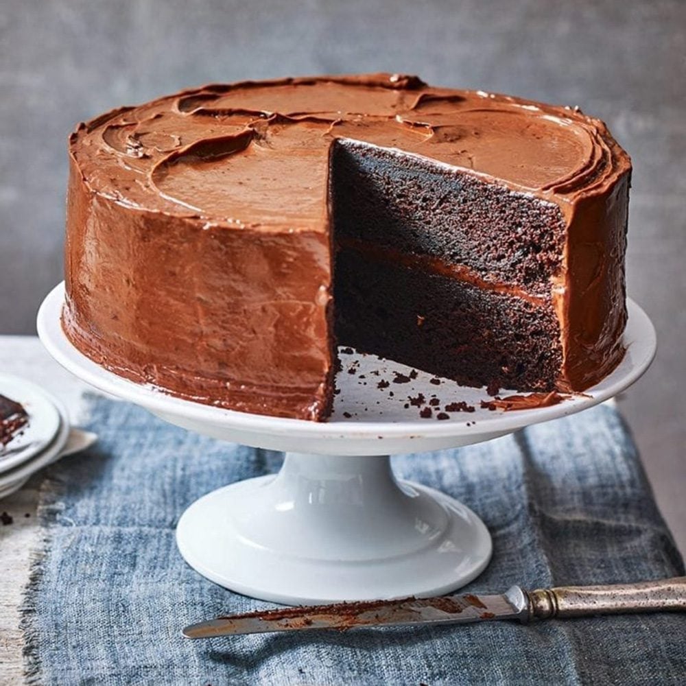 A large chocolate cake on a cake stand, with a slice removed