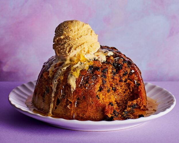 A steamed spotted dick pudding on a plate, with a large scoop of ice cream melting over the top