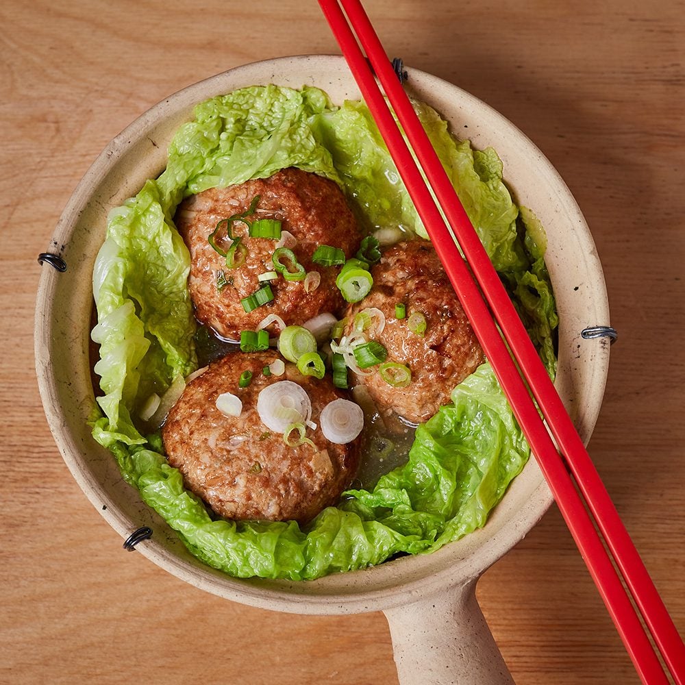 A clay pot of three large meatballs surrounded by Chinese cabbage leaves, with a pair of red chopsticks resting on top