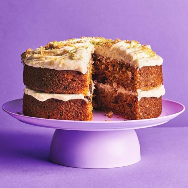 A large carrot cake on a purple background with a slice removed