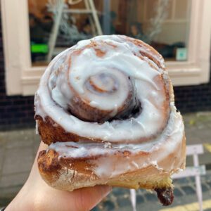 A cinnamon bun being held aloft, coated in white icing