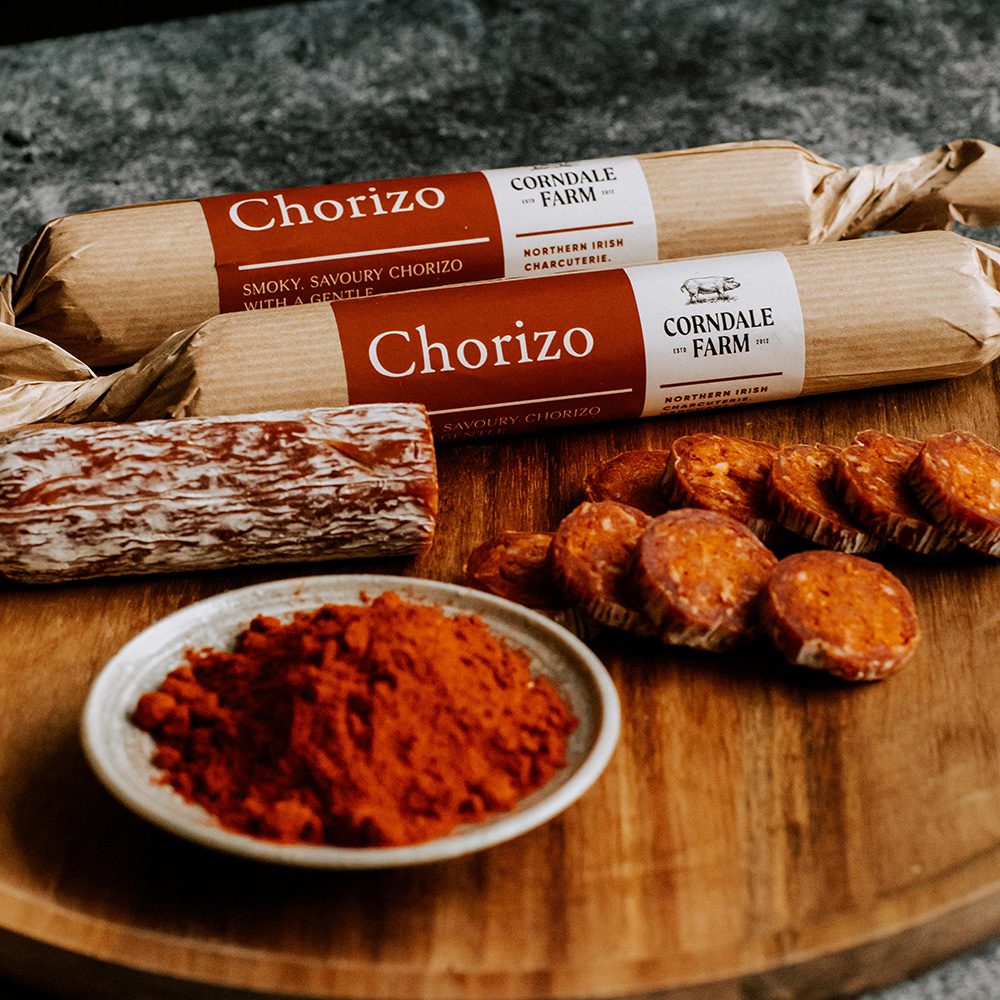 Two chorizo from Corndale Farm in brown paper packaging, with a dish of spices and sliced chorizo in the foreground