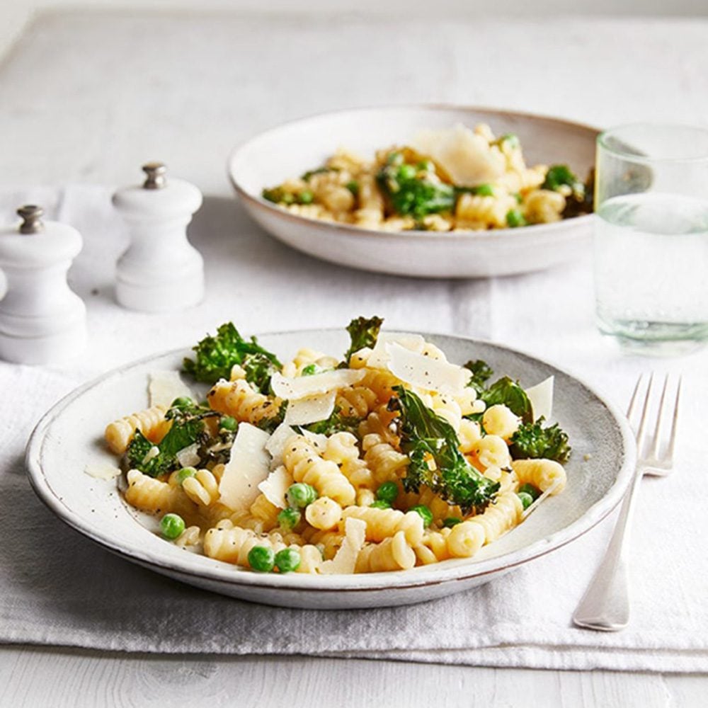 Two plates of pasta with peas, kale, garlic and cheese