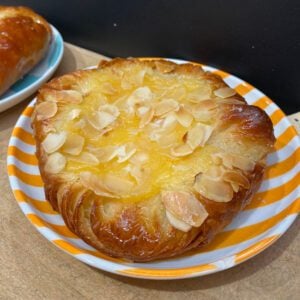 A pastry with a pool of yellow custard in the centre and flaked almonds on top