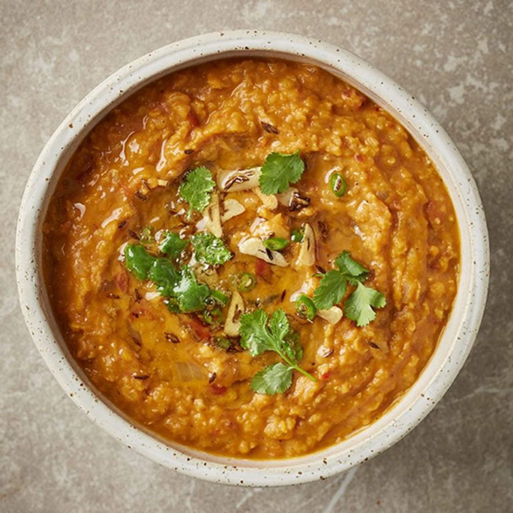 A bowl of red lentil dal topped with herbs