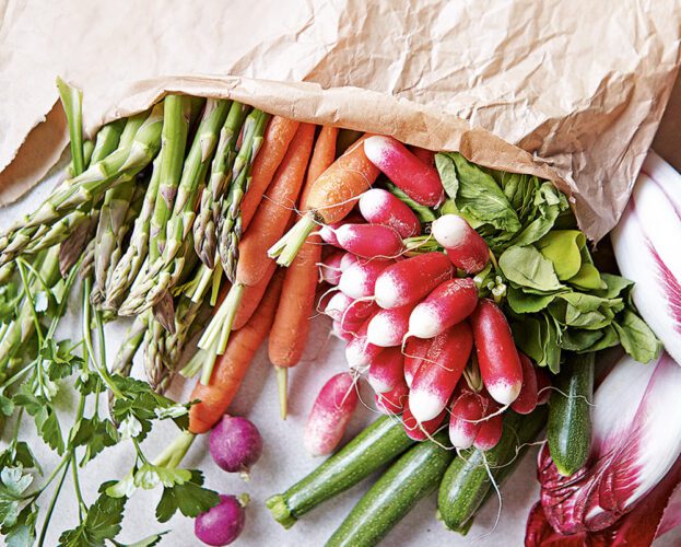 Fresh vegetables spilling out of a brown paper shopping bag