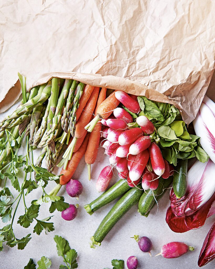 Fresh vegetables spilling out of a brown paper shopping bag