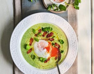 Overhead view of watercress soup in a bowl, topped with lardons and poached eggs