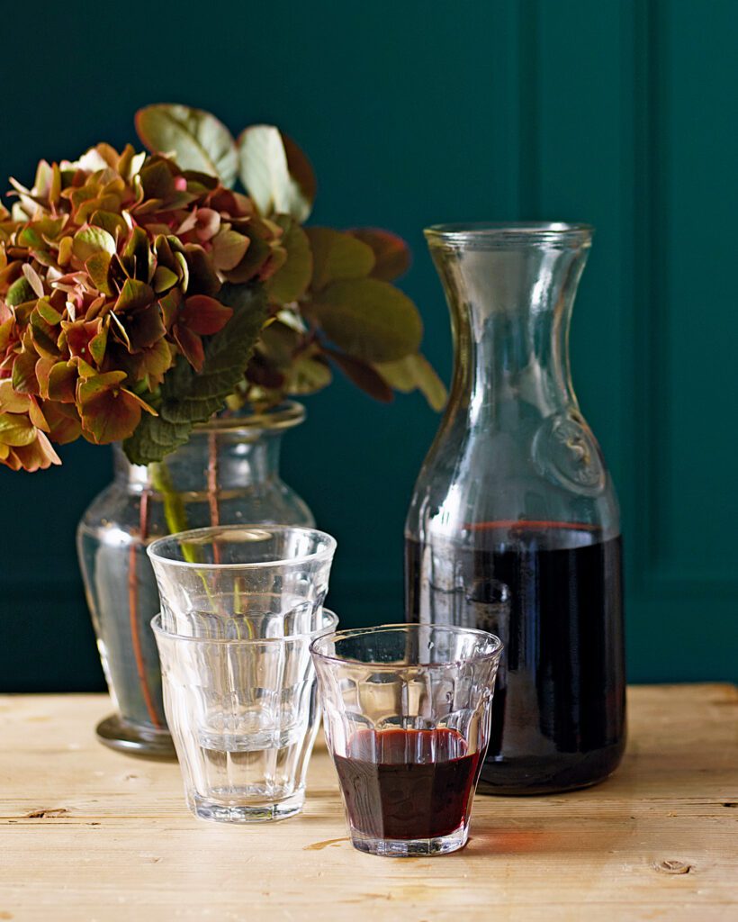 A carafe of red wine with a filled glass in the foregound
