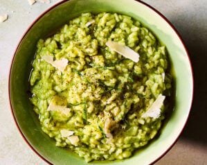 An overhead view of a bowl of green wild garlic risotto with shards of parmesan on top