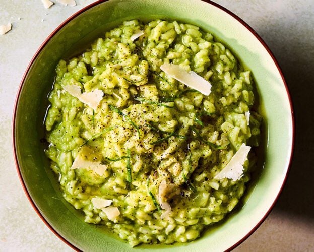 An overhead view of a bowl of green wild garlic risotto with shards of parmesan on top
