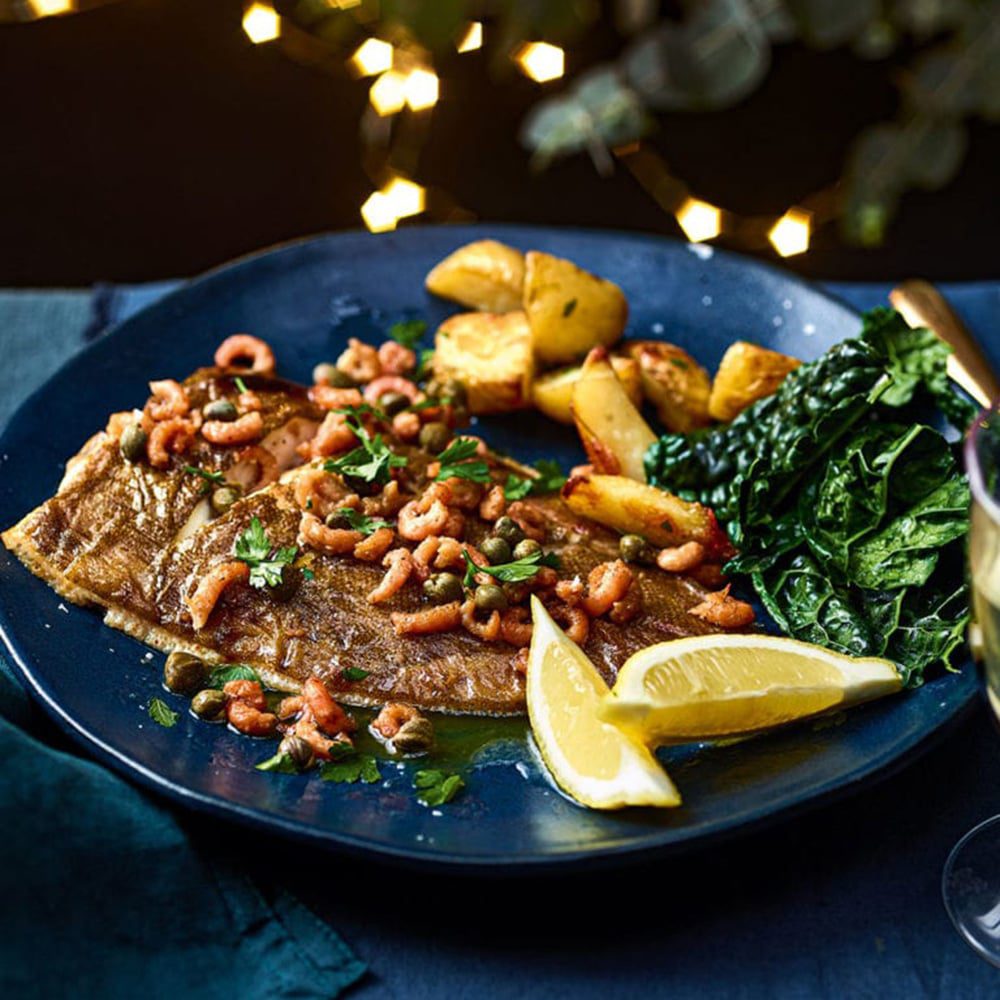 Lemon sole on a platter topped with potted shrimp butter and lemon wedges on the side